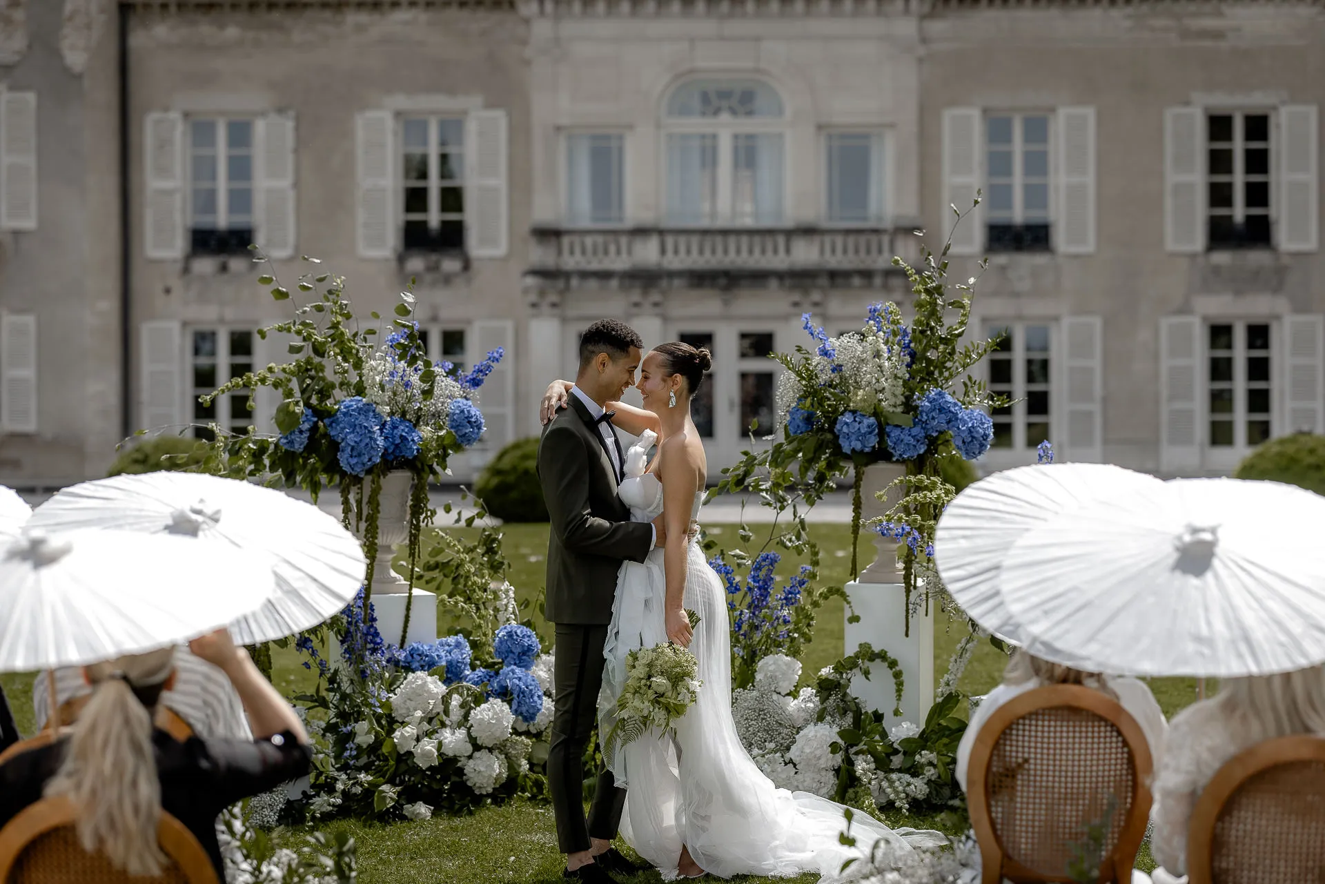 Romantic wedding ceremony at Chateau de Varennes with bridal couple under floral arch and white parasols
